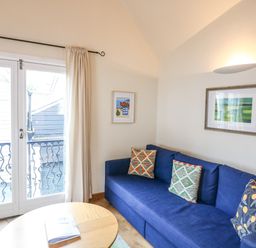 A living room with a blue sofa and patterned cushions near glass doors with curtains at The Loft Cottage in Totnes