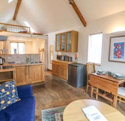 A small kitchen and dining area with wooden cabinets a blue sofa and a loft space at The Loft Cottage in Totnes