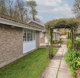 A walkway with a wooden arch and greenery between stone and brick buildings at Badger Sett in Granite Henge near Looe near Polperro