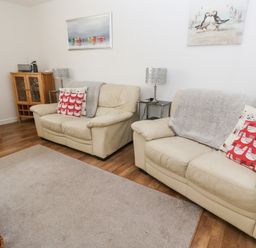 A living room with two beige sofas and red patterned cushions at Badger Sett in Granite Henge near Looe