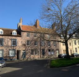 A street with rows of traditional houses with chimneys and parked cars along a road with a tree in the foreground at The Indigo House in Berwick-Upon-Tweed