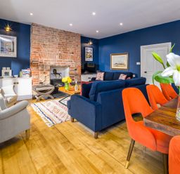 A living room with blue walls a brick fireplace blue sofas orange chairs and wooden floor at The Indigo House in Berwick-Upon-Tweed