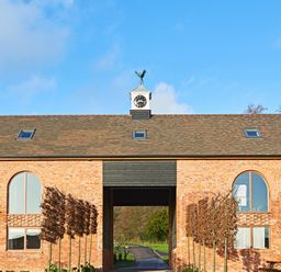 A brick building with arched windows a clock tower and a central open passage at The Millhouse in Ledbury near Welland