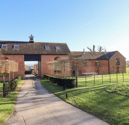 A paved driveway leading to a brick building with a clock tower and fenced lawns at The Millhouse in Ledbury near Welland