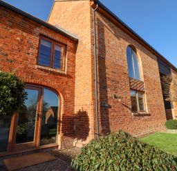The exterior of a brick house with arched glass doors and windows and plants in front at The Millhouse in Ledbury near Welland