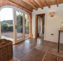 An entryway with stone tile flooring a wicker basket a small table with a glass cloche wall lights and arched glass doors at The Millhouse in Ledbury near Welland
