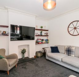 A living room with a gray sofa and armchair a wall-mounted tv and shelves with books and decorations at Castle Manor in Scarborough