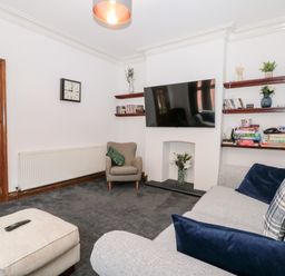 A living room with a wall-mounted television a gray sofa and armchair shelves with books and board games at Castle Manor in Scarborough