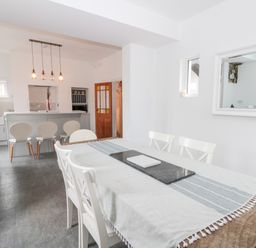 A dining area with a wooden table and white chairs next to a kitchen with a breakfast bar and stools at Castle Manor in Scarborough