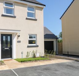 Front view of a beige house with black door and windows next to a garage and driveway at Pebble Bay in Appledore
