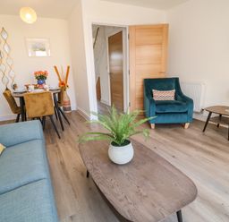 A living room with a blue couch a teal armchair a wooden coffee table with a plant and a dining table with four chairs at Pebble Bay in Appledore