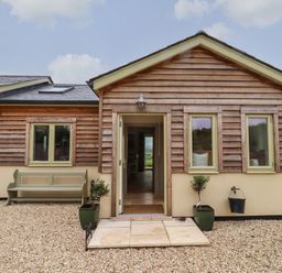 A house exterior with wooden siding windows a bench and two potted plants at Cotswold View in Shipton Under Wychwood
