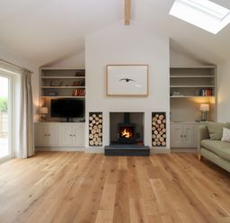 A living room with a fireplace wood stacks bookshelves a television a sofa and sliding glass doors at Cotswold View in Shipton Under Wychwood