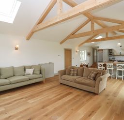 An open living room and kitchen with wooden beams on the ceiling two sofas and a kitchen island with stools at Cotswold View in Shipton Under Wychwood