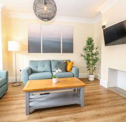 A living room with blue sofas a wooden coffee table and a wall-mounted TV at Seaside House in Gorleston-On-Sea