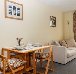 A dining table with two chairs and plates next to a sofa with cushions and a floor lamp at Mabel's View in East Allington Devon
