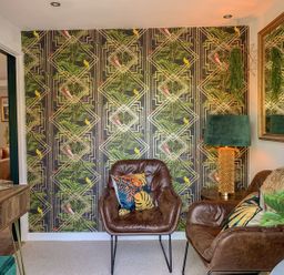 A small sitting area with two brown leather chairs, a green lampshade on a side table, a large mirror, patterned wallpaper, and indoor plants at Inny Brook Burrow in Davidstow near Camelford
