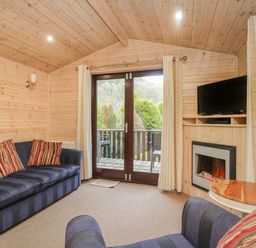 A living room with blue striped sofas red striped cushions a wooden round table a wall mounted tv an electric fireplace and glass doors leading outside at Canadian Cabin No 39 in Keswick
