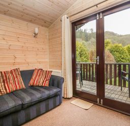 A room with a dark striped sofa with striped cushions wood paneled walls and glass doors leading to a balcony with chairs at Canadian Cabin No 39 in Keswick
