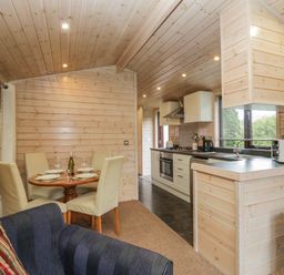 A kitchen and dining area with wooden walls and ceiling and a small round dining table with four chairs at Canadian Cabin No 39 in Keswick