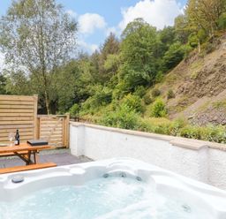 A hot tub and table with drinks in an outdoor area at Riverside Cottage No 4 Keswick