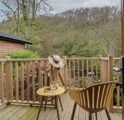 A wooden balcony with a chair a small table holding a bottle and two glasses and a hat hanging on the railing at Pod No 28 in Keswick