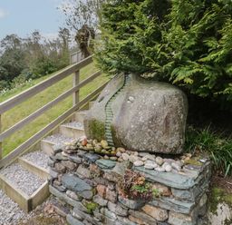A stone sculpture on a rock wall next to wooden steps and greenery at Pod No 28 in Keswick