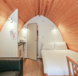 A small room with a bed sofa kitchenette and wooden ceilings at Pod No 28 in Keswick