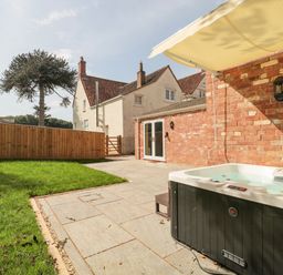 An outdoor patio with a hot tub grass lawn and a brick building at The Nest in North Petherton