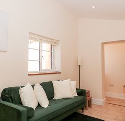 A room with a green sofa and white pillows a wooden dining table with chairs and a window at The Nest in North Petherton