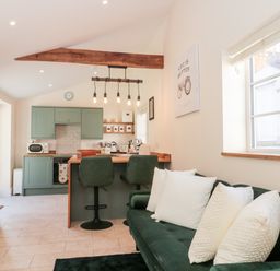 A kitchen with green cabinets and bar stools next to a dark green sofa with white pillows at The Nest in North Petherton