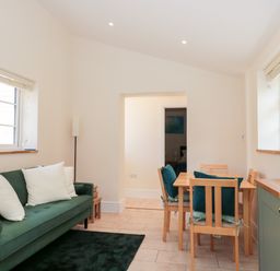 A living room with a green sofa and white cushions next to a wooden dining table with chairs at The Nest in North Petherton