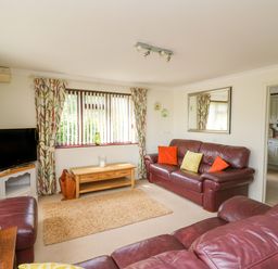 A living room with leather sofas a wooden coffee table a television and a window with patterned curtains at The Clove in Poyston Cross near Haverfordwest