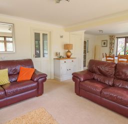 A living room with two brown leather sofas a white cabinet with a lamp and a dining area with a wooden table and chairs at The Clove in Poyston Cross near Haverfordwest