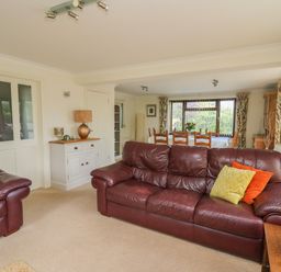A living room with leather sofas and a wooden dining table near windows at The Clove in Poyston Cross near Haverfordwest