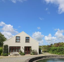 A building with windows and a bench outside near a round pond and greenery at The Clove in Poyston Cross near Haverfordwest