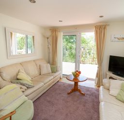 A living room with beige sofas a round wooden table with fruit and sliding glass doors at Lavender Lodge in Haverfordwest