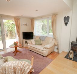 A living room with cream sofas a wooden coffee table a television and a wood burning stove at Lavender Lodge in Haverfordwest