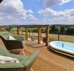 A wooden deck with two green armchairs a bottle a hot tub with water and a rural landscape at The Coop in Aston near Woore
