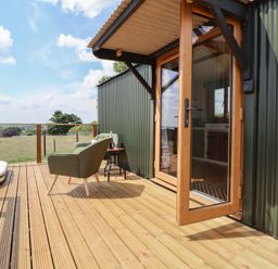 A wooden deck with a green chair small table and glass door at The Coop in Aston near Woore