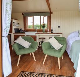 A small room with two green chairs, a bed, kitchen area with sink and stools at The Coop in Aston near Woore