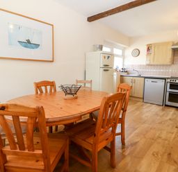 A kitchen with wooden dining table and chairs a refrigerator stove dishwasher and cabinets at Jacuma in Rhosneigr
