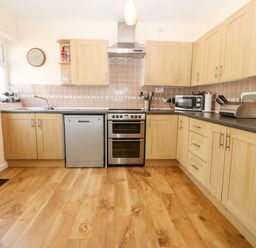 A kitchen with wooden cabinets a dishwasher stove microwave and wooden floor at Jacuma in Rhosneigr