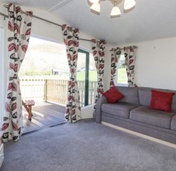 A living room with a gray sofa and red cushions near sliding glass doors with patterned curtains overlooking a wooden deck at Swinside in Lorton