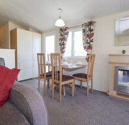 A dining area with a wooden table and four chairs near a window with patterned curtains and a fireplace in the corner at Swinside in Lorton