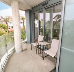 A balcony with two chairs and a small table overlooking trees and buildings at Sebastians View in Falmouth