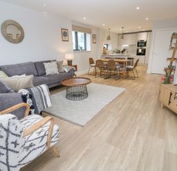 An open plan living room and kitchen with a grey sofa an armchair and a dining table at Sebastian's View in Falmouth