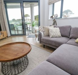 A living room with a grey sofa coffee table television and sliding glass door leading to a balcony at Sebastian's View in Falmouth