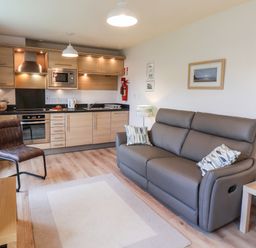 A kitchen and living area with wooden cabinets grey sofa and a chair at Kittiwakes The Bay - Filey