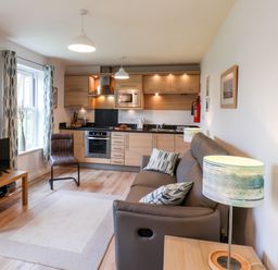 An open plan living room and kitchen with a sofa, armchair, television, wooden cabinets, and kitchen appliances at Kittiwakes in The Bay - Filey